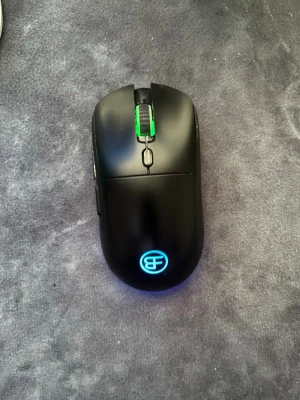 Svart gamingmus med RGB-belysning - Säljer en svart gamingmus med RGB-belysning och två sidoknappar. Musen har en stilren design med ett upplyst logotyp på ovansidan och ett scrollhjul med grön belysning. Perfekt för gaming eller arbete vid datorn.