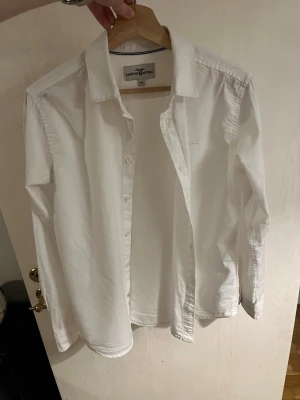 Vit skjorta från Hampton Republic - Klassisk vit skjorta från Hampton Republic med krage och knäppning framtill. Skjortan är långärmad och har en stilren, tidlös design i mjuk bomull. Perfekt att styla till olika looks och enkel att matcha med det mesta.