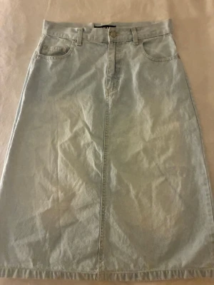 Ljusblå lång jeanskjol - Säljer en klassisk ljusblå lång jeanskjol med femficksmodell och knappgylf. Kjolen har bälteshällor och raka sömmar framtill och baktill. Perfekt för dig som gillar enkel och tidlös denimstil. Går säkert att sy om till en kortare kjol om man föredrar de❤️