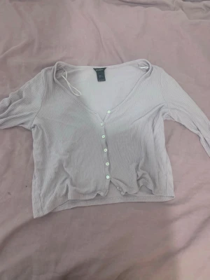 Ljuslila ribbad croppad topp Gina Tricot - Trendig ljuslila croppad topp med ribbad struktur. Toppen har v-ringning, knappar framtill och trekvartsärm. Perfekt att styla med höga jeans eller kjol för en cool look.