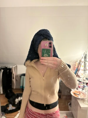 Beige zip-up hoodie med fuskpäls - prislapp på den,! Säljer en beige zip-up hoodie med fuskpäls på huvan. Tröjan är ribbstickad med långa ärmar och har en kort, croppad passform. Perfekt för dig som gillar trendiga och mysiga plagg med lite extra detaljer.