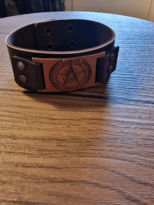 Armband vintage pentagram - Svart läderarmband med ett detaljerat pentagram i metall. Armbandet har justerbara tryckknappar för att passa olika handledsstorlekar. Storlek 23 cm långt. Bredd 3 cm.