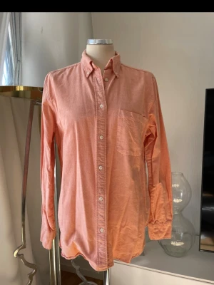 Skjorta orange 36/38 - Snygg  skjorta i bomull med klassisk krage, bröstficka och knappar framtill. Skjortan har lång ärm med knapp vid manschetten och en relaxed passform. Perfekt för dig som gillar en chill och trendig stil.