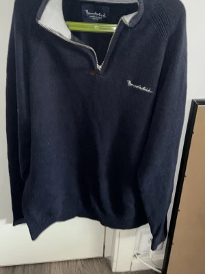 Mörkblå halvzip-tröja från Brookfield - Mörkblå stickad tröja från Brookfield med halvzip och ljusgrå insida på kragen. Tröjan har broderad logga på bröstet och ribbade muddar. Perfekt för lager-på-lager och chill stil.