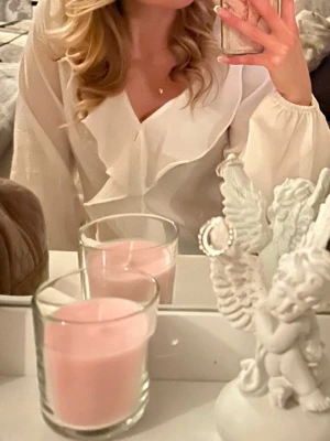 Vit blus med volang och v-ringning - Säljer en super söt vit blus med v-ringning och stora volangdetaljer framtill. Blusen har långa ärmar med lätt puff