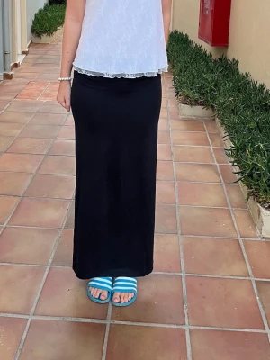 Svart långkjol med slits - Säljer en svart långkjol med en snygg slits på sidan. Kjolen har en rak och enkel passform som ger en clean look. Perfekt att matcha med crop tops eller oversized tröjor. Materialet känns mjukt och stretchigt, vilket gör den bekväm att bära.