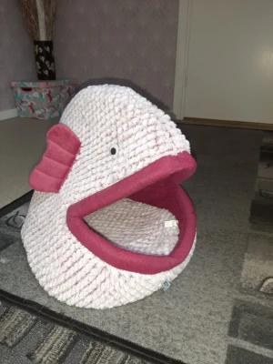 Rosa fiskformad kattbädd - Unik kattbädd formad som en fisk i mjuk, stickad textil. Utsidan är ljusrosa med mörkrosa detaljer på fenor och insida av munnen. Bädden har en stor öppning framtill och ett gulligt öga på sidan. Perfekt för dig som vill ge din katt en mysig och rolig plats att vila på.