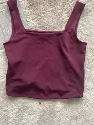 Vinröd linnetopp från Amisu - Snygg vinröd linnetopp från Amisu med breda axelband och rak halsringning. Toppen är ärmlös och har en croppad passform som passar perfekt till höga jeans eller kjol. Tillverkad i mjuk bomull för en bekväm känsla. Lappen e upp o ner. Andvänds 4 gånger typ💕🫰🏼