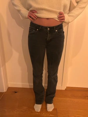 Mörkgrå bootcut jeans - Säljer ett par mörkgrå bootcut jeans med klassisk femficksdesign och normalhög midja. Jeansen har vita sömmar och stängs med knapp och dragkedja. Materialet är mjukt och stretchigt för skön passform.