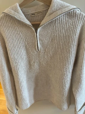 Beige stickad tröja med dragkedja - Mysig beige stickad tröja från Pull&Bear köpt via Zalando med ribbad struktur och halv dragkedja framtill. Tröjan har hög krage som kan vikas ner och långa ärmar. Perfekt för lager på lager och chill stil. Materialet känns mjukt och värmande.