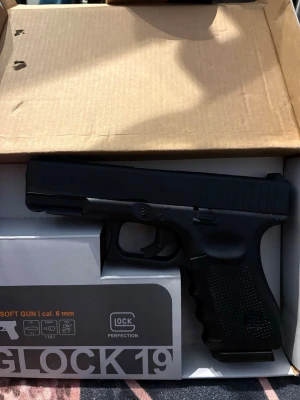 Svart airsoftpistol Glock 19 Gen 4 - Säljer en svart airsoftpistol Glock 19 Gen 4 i plast, kaliber 6 mm. Pistolen har realistisk design med detaljerad märkning och greppvänligt handtag. Perfekt för airsoftspel eller som samlarobjekt. Levereras i originalkartong.