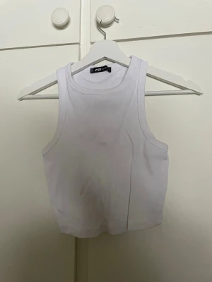 Vit ribbad linnetopp från FB Sister - Säljer en enkel och fräsch vit ribbad linnetopp från FB Sister. Toppen är ärmlös med rund halsringning och croppad passform, perfekt till jeans sopm till kjol. Materialet är mjukt och stretchigt för en bekväm känsla.