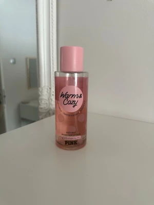 Warm & Cozy Body Mist från PINK - Fräsch body mist från PINK i doften Warm & Cozy med inslag av toasted coconut och passionfruit. Flaskan är cylinderformad i plast med rosa detaljer och prickigt mönster. Perfekt för dig som gillar söta och tropiska dofter.