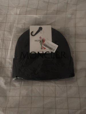Svart Moncler mössa - Svart Moncler mössa, väldigt snygg och fräsch. Klassisk och stilren design som passar perfekt till höstens och vinterns outfits. Mössan är tillverkad i mjukt material för extra komfort.