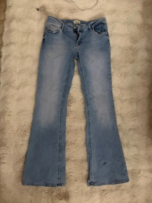 Ljusblå bootcut jeans från Only - Ljusblå jeans från Only med bootcut passform och klassisk femficksdesign. Jeansen har en lätt utsvängd nederdel och subtila slitningar för en avslappnad look. Perfekta för dig som gillar retrostil och vill ha ett par bekväma jeans i bomull.