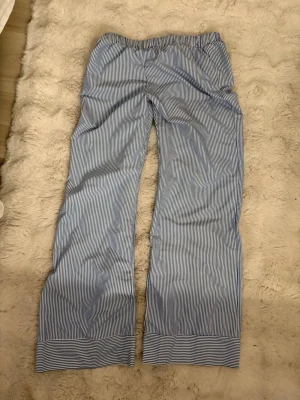 Randiga pyjamasbyxor i blått och vitt - Klassiska pyjamasbyxor med blå och vita smala ränder. Byxorna har rak passform, resår i midjan och bredare randig kant längst ner vid bensluten. Perfekta för en avslappnad kväll hemma.