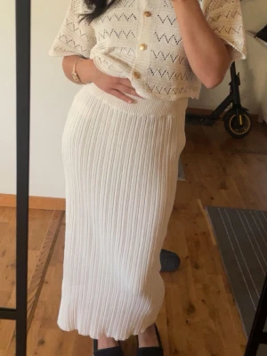 Vit ribbad långkjol - Säljer en snygg vit långkjol med ribbad struktur. Kjolen har en hög midja och är figurnära med en mjuk och stretchig känsla. Perfekt att styla med en stickad topp eller t-shirt för en trendig look.