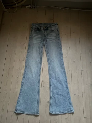 Ljusblå bootcutjeans från weekday - Säljer ett par ljusblå bootcutjeans från weekday med klassisk femficksdesign och utsvängda ben. Jeansen har en grön patch med logga bak i midjan och är tillverkade i denim med lätt tvättad look. Perfekta för dig som gillar retrostil och vill sticka ut.