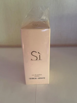 Giorgio Armani Sì Eau de Parfum - Giorgio Armani Sì Eau de Parfum i en elegant ljusrosa kartong med stilren svart text. Parfymen kommer i en rektangulär förpackning av kartong och är inslagen i plast. Perfekt för dig som gillar lyxiga och feminina dofter.