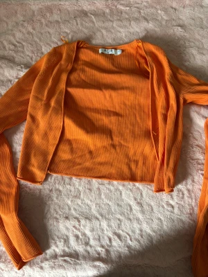 Ribbad orange kofta från NA-KD - Trendig orange ribbad kofta från NA-KD med öppen front och långa ärmar. Kortare modell som passar perfekt till jeans eller kjol. Tillverkad i mjukt, stretchigt material för en bekväm och snygg look.