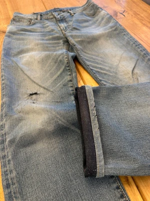 Levi’s 5-Pocket Jeans (W30 L32) 🇯🇵 - Levi’s 5-Pocket Jeans (W30 L32) 🇯🇵 Heavily distressed light wash with pale blue tones, strong fading & natural creasing throughout • Large knee blowout with frayed edges • Signature red tab, copper rivets & contrast stitching • “Water<Less” tagged • Straight fit, relaxed drape • Raw frayed hems Bold vintage piece with real worn-in character  Feel free to ask for more details! (6)
