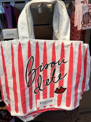 Randig shoppingväska från Kérastase - Två snygga tygväskor/strandväakor från Kérastase med breda axelband. Ena väskan har vita och rosa ränder, texten 'Bisou d'été' och en liten läppillustration. Den andra har vita och gula ränder. Båda är rymliga och perfekta för shopping eller stranden.