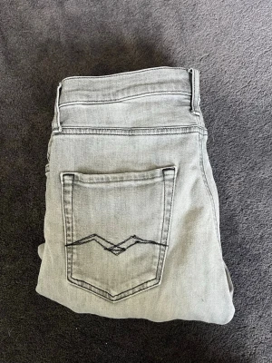 Grå jeans från Replay - Snygga grå jeans från Replay med klassisk femficksdesign och cool broderad detalj på bakfickan. Jeansen har dragkedjegylf och bälteshällor. Perfekta för dig som gillar en stilren och avslappnad look.