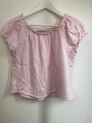 Ljusrosa blus med kort ärm - Söt ljusrosa blus med korta ärmar och rynkad resår vid halsringningen. Luftig och lätt i materialet, perfekt för varma dagar. Passar till både jeans och kjol för en avslappnad look.