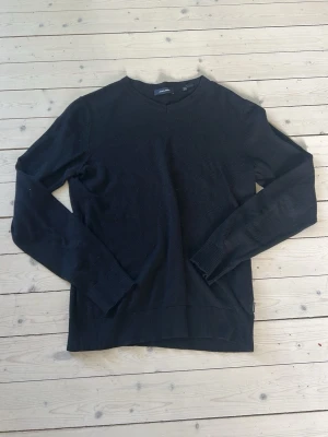 Svart stickad tröja Jack & Jones - En stilren svart stickad tröja från Jack & Jones med V-ringning och långa ärmar. Tröjan har ribbade muddar vid ärmslut och nederkant, vilket ger en snygg passform. Perfekt att matcha med jeans eller chinos för en clean look.