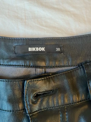 Svarta skinnjeans från BikBok - Snygga svarta jeans i skinn från BikBok. Modellen har klassisk femficksdesign och raka ben. Passa perfekt med en snygg spex tröja( finns i min shop). Stängs med knapp och dragkedja.