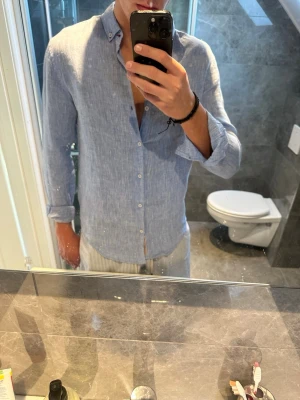 Ljusblå linneskjorta med knappar - Säljer en riktigt snygg linneskjorta i ljusblått från Zara. Skjortan är i bra skick och passar perfekt nu till sommaren.Jag på bilden är 188cm. Hör av er vid vidare frågor och ch funderingar:)