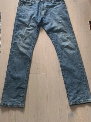 Blå raka jeans med slitningar - Ett par klassiska blå jeans med rak passform och diskreta slitningar framtill. Jeansen har fem fickor och normal midja. Perfekta för en avslappnad och trendig look. Materialet är denim i bomull.