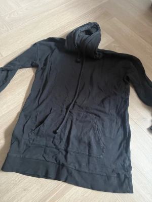 Svart hoodie med magficka - Svart hoodie med klassisk huva och dragsko. Har en stor magficka framtill och långa ärmar. Tillverkad i mjukt bomullstyg, perfekt för en avslappnad stil. Enkel och stilren design utan tryck eller logga.