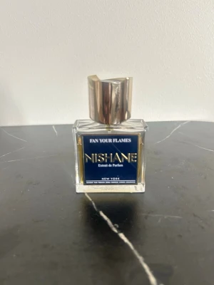 Nishane Fan Your Flames parfym - Exklusiv parfym från Nishane, Fan Your Flames, i en stilren fyrkantig glasflaska med mörkblå etikett och elegant guldigt lock. En lyxig doft som sticker ut och passar dig som vill ha något unikt. Endast 35/50 ml kvar