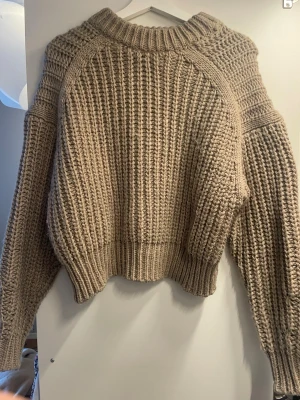 Beige chunky stickad tröja - Säljer en beige chunky stickad tröja med grov struktur och bred ribbad mudd vid ärmslut och nederkant. Tröjan har en avslappnad passform, rund halsringning och långa ärmar. Perfekt för kalla dagar och superenkel att styla till jeans eller kjol.