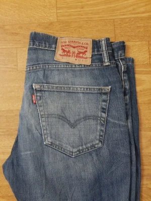 Levi's 511 blå jeans - Säljer ett par klassiska blå Levi's 511 jeans med normal passform och femficksdesign. Jeansen har en snygg tvättad look, ikonisk läderpatch bak och röd Levi's-tag på bakfickan. Perfekta för en avslappnad stil och tillverkade i slitstarkt denim.