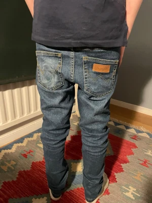 Blå jeans från Wrangler - Säljer ett par klassiska blå jeans från Wrangler med raka ben och snygga detaljer på bakfickorna. Jeansen har normal midja och är tillverkade i slitstark denim. Perfekta för en avslappnad och cool stil. Och Grisch