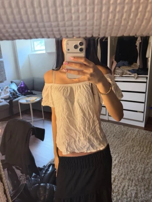 Vit offshoulder topp med kort ärm - Söt vit offshoulder topp med korta ärmar och rynkad resår upptill. Luftig och lätt i materialet, perfekt för varma dagar. Enkel och stilren design som är lätt att matcha med olika outfits.