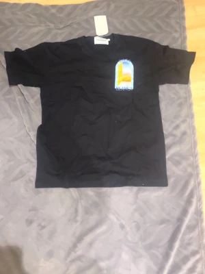 Svart t-shirt från Casablanca - Svart t-shirt från Casablanca med rund hals och tryck på bröstet i blått, gult och orange. Trycket föreställer en dörr med texten 'Casa Blanca'. T-shirten är i bomull och har en klassisk passform.