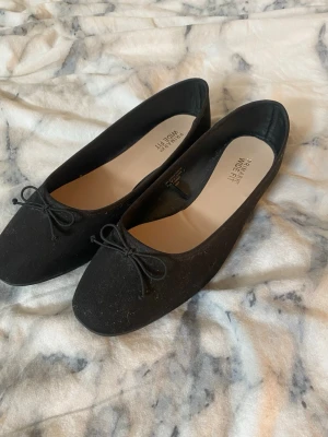 Svarta ballerinaskor med rosett - Stilrena svarta ballerinaskor från primemark med klassisk rund tå och söt rosettdetalj framtill. Skorna har en mjuk ovandel i textil och en platt sula i gummi för extra komfort. Perfekta för en enkel och snygg look.