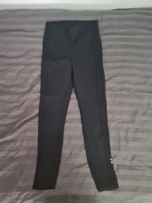Svarta sportleggings med dragsko - Svarta sportleggings med hög midja och justerbar dragsko i midjan. En ficka på varje sida av benet. Tight passform och långa ben, perfekt för träning eller chill. Liten logga vid benslutet. Materialet är stretchigt och följsamt för maximal rörelsefrihet.