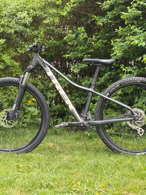 Svart mountainbike från Trek - Säljer en svart mountainbike från Trek med robust ram, grova däck och skivbromsar. Cykeln har en sportig design och är perfekt för dig som gillar att cykla i skogen eller på tuffare underlag. Ramen är i metall och Trek-loggan syns tydligt på sidan.