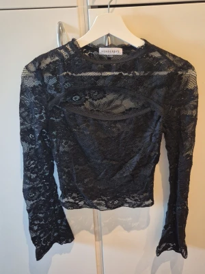 Svart spetsblus från Venderby's - Säljer en svart långärmad spetsblus från Venderby's i storlek S/M. Blusen har transparent spets med blommönster, rund halsringning och figurnära passform. Utskuren detalj framtill. Storlek S/M.