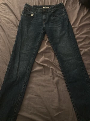 Mörkblå raka jeans - Snygga mörkblå jeans med rak passform och klassiska fem fickor. Jeansen har diskreta slitningar och kontrastsömmar, samt bakfickor med dekorativ söm. Perfekta för en avslappnad och stilren look.