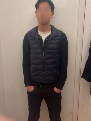 Mörkblå dunväst från Polo Ralph Lauren - Snygg mörkblå dunväst från Polo Ralph Lauren med diskret röd logga på bröstet. Västen har dragkedja framtill och quiltad design som ger en modern look. Västen är i toppskick, inga hål eller märken. Klassisk och stilren modell. Nypris runt 3000. Storleken passar 165-175cm och runt 50-60kg. Den är naturligtvis äkta.