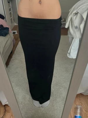 Svart långkjol i stretchigt material med ett slit - Säljer en svart långkjol med tight passform och hög midja. Kjolen är enkel och stilren utan mönster eller detaljer, perfekt för dig som gillar minimalistisk stil. Materialet känns stretchigt och följsamt.