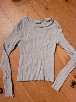 Ljusgrå ribbad långärmad topp - En stilren ljusgrå ribbad topp med lång ärm och rund halsringning. Toppen har en slim passform och är perfekt att matcha med jeans eller kjol. Materialet är mjukt och stretchigt för en bekväm känsla.