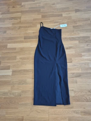 Svart oneshoulder klänning NA-KD - Snygg svart oneshoulder klänning från NA-KD med smal axelrem och hög slits på sidan. Storlek 36. 