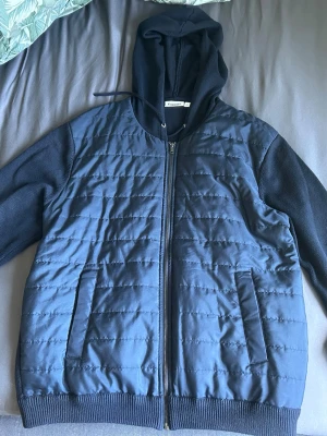 Mörkblå hoodie med quiltad front  - Snygg mörkblå hoodie från kappahl med quiltad front och ärmar i mjukt tyg. Dragkedja hela vägen, två fickor fram och ribbade muddar. Perfekt för en chill och stilren look. Hör av dig vid minsta fundering 😊