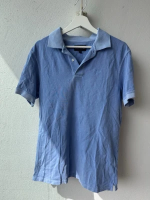 Ljusblå pikétröja från Barbour - Snygg ljusblå pikétröja från Barbour med klassisk krage och knappar framtill. Tröjan har korta ärmar och broderad logga på bröstet. Perfekt för en avslappnad och stilren look. använd 2 gånger om ens så mycket (9.75/10)
